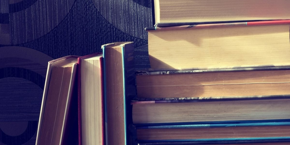 Stack of fantasy and science fiction books on a wooden table with a warm lamp