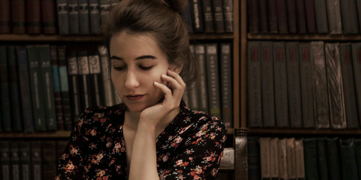 A person contemplates a shelf of books, considering where to start their reading journey with a complex author.